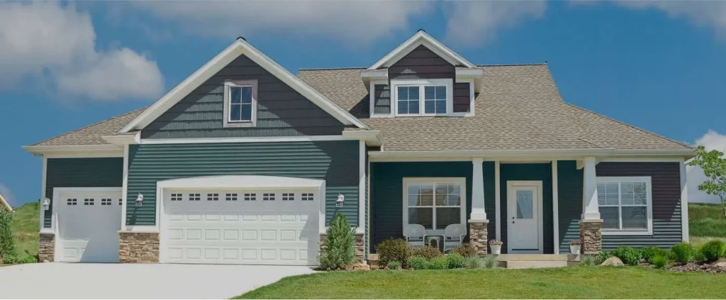 A modern, two-story suburban house in NJ with dark green siding, white trim, a double garage, large windows, and a covered front porch—perfect inspiration for any Roofing Contractor Monmouth County project. Blue sky and green lawn complete the scene.