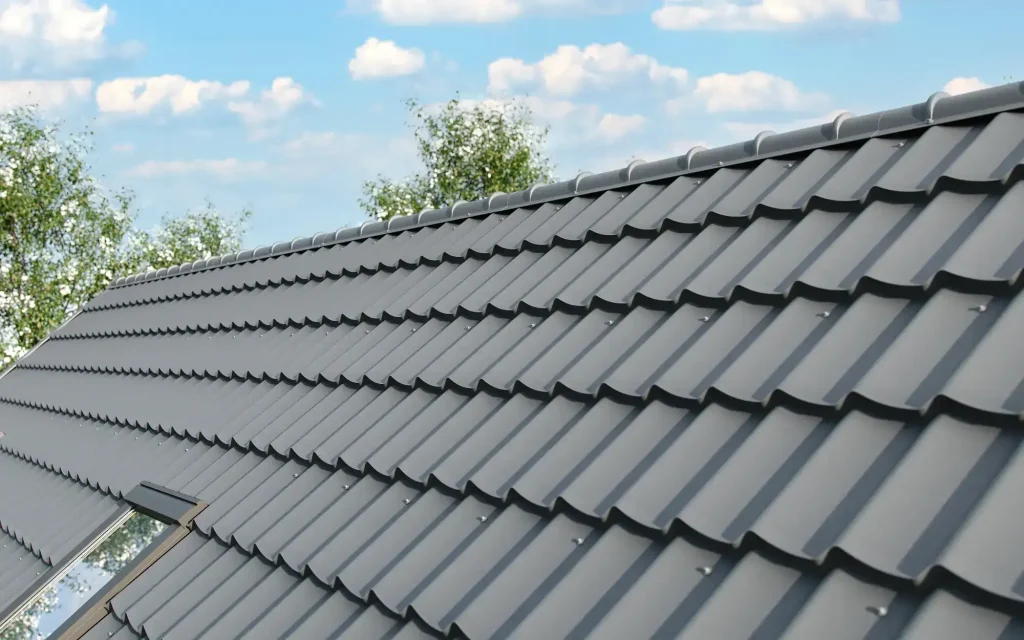Close-up view of a sloped roof with gray metal roof tiles and a skylight, expertly installed by a trusted roofing contractor in Monmouth County, NJ, with trees and blue sky with clouds in the background.
