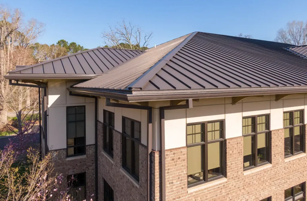 A close-up view of a modern building with a brown metal sloped roof by a top Roofing Contractor Monmouth County, featuring large windows and brick walls, taken on a clear, sunny day with trees in the background in NJ.