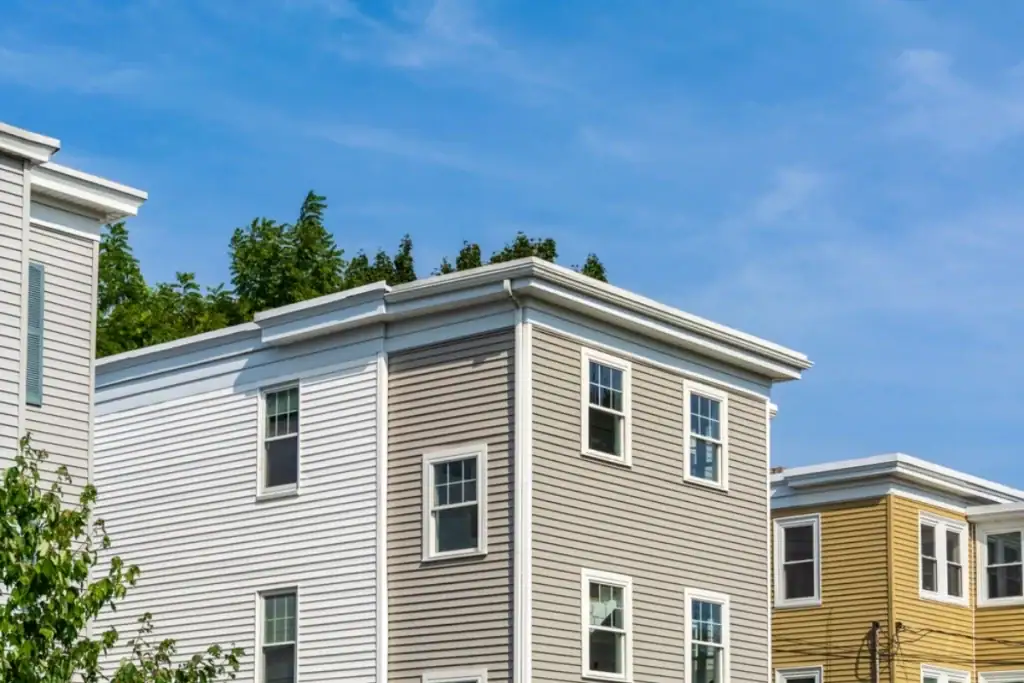 Three modern townhouses with beige, white, and yellow siding stand side by side under a clear blue sky in Monmouth County, NJ—perfect homes for anyone seeking a trusted roofing contractor in the area. Trees are visible in the background.