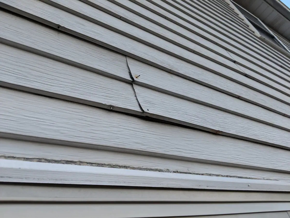 Close-up of a house’s exterior siding in NJ, showing warped panels with gaps between them—signs of damage or improper installation that a Roofing Contractor Monmouth County can address.