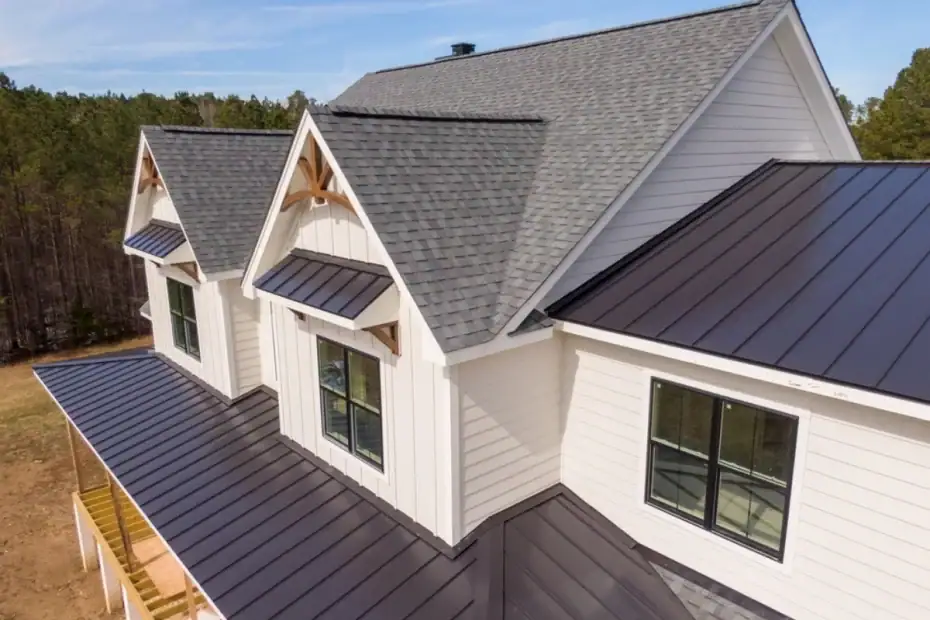 A modern house with light siding, black framed windows, gray asphalt shingles on the upper story, and a black metal porch roof—expertly crafted by a top Roofing Contractor in Monmouth County, NJ—nestled among trees under a clear blue sky.