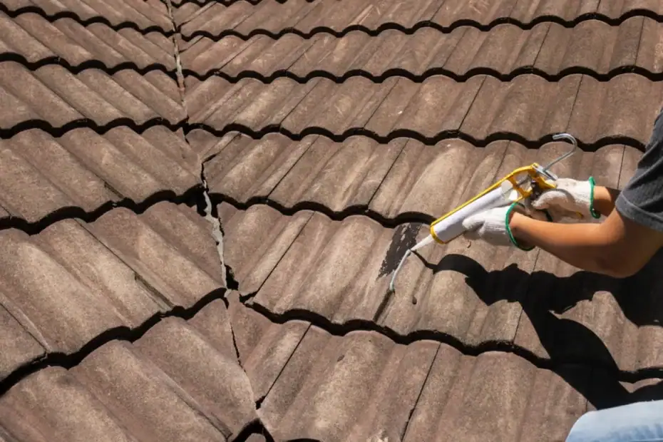 A Roofing Contractor Monmouth County, NJ, wearing gloves applies sealant to a large crack in a brown tiled roof using a caulking gun, repairing the damaged section under sunlight.