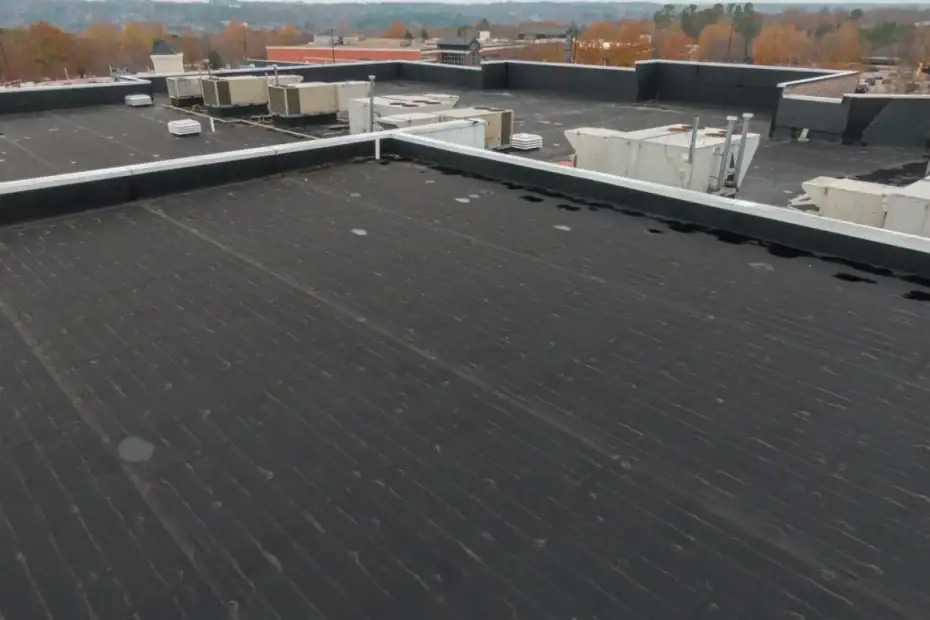 Flat black rooftop with several HVAC units and vents, surrounded by parapet walls. In the background, NJ trees with autumn foliage and distant buildings under an overcast sky, ideal for a Roofing Contractor Monmouth County project.